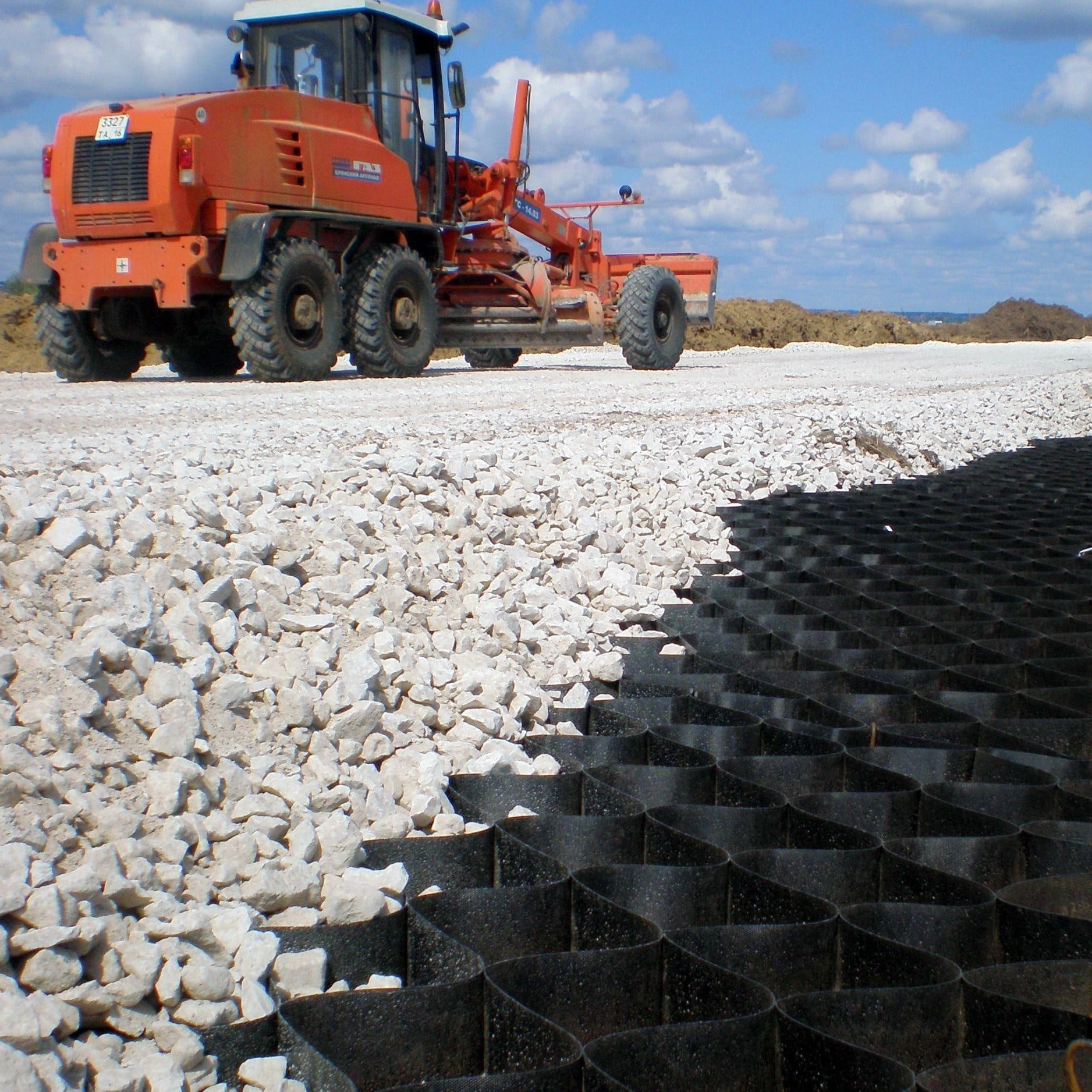 HDPE geocell with gravel infill for road base stabilization, installed with motor grader on construction site