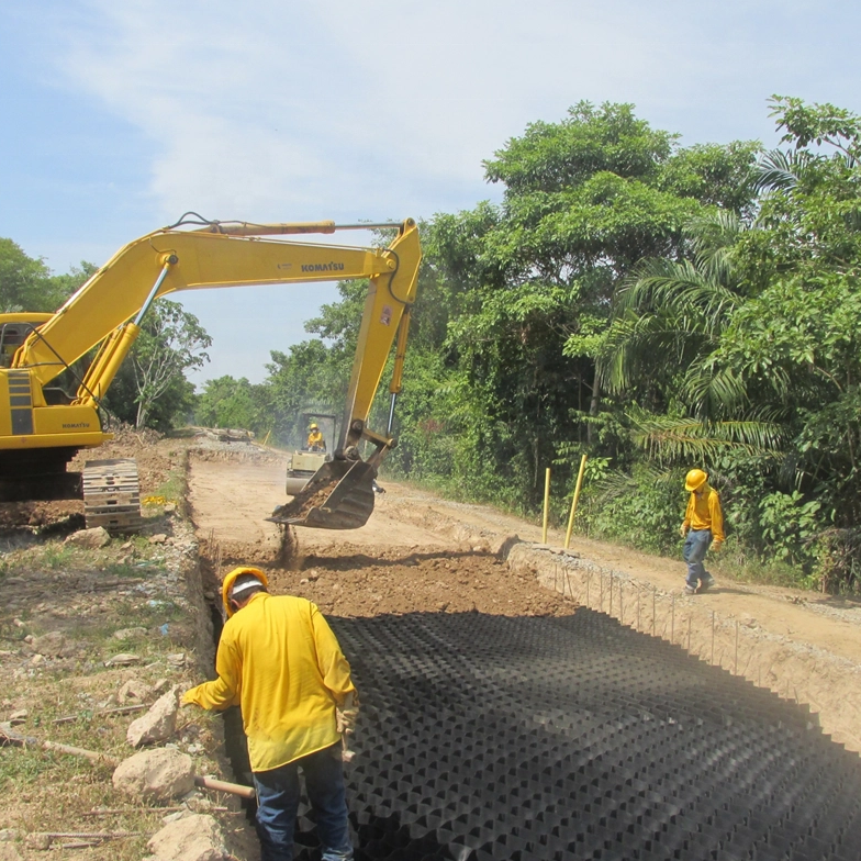Workers installing black HDPE geocell on roadside slope with excavator for soil retention and erosion prevention