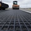 Fiberglass geogrid being installed on highway subgrade with roller compactor, for new road construction