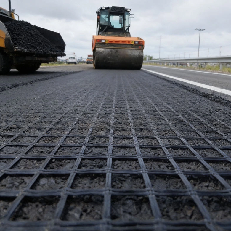 Fiberglass geogrid being installed on highway subgrade with roller compactor, for new road construction